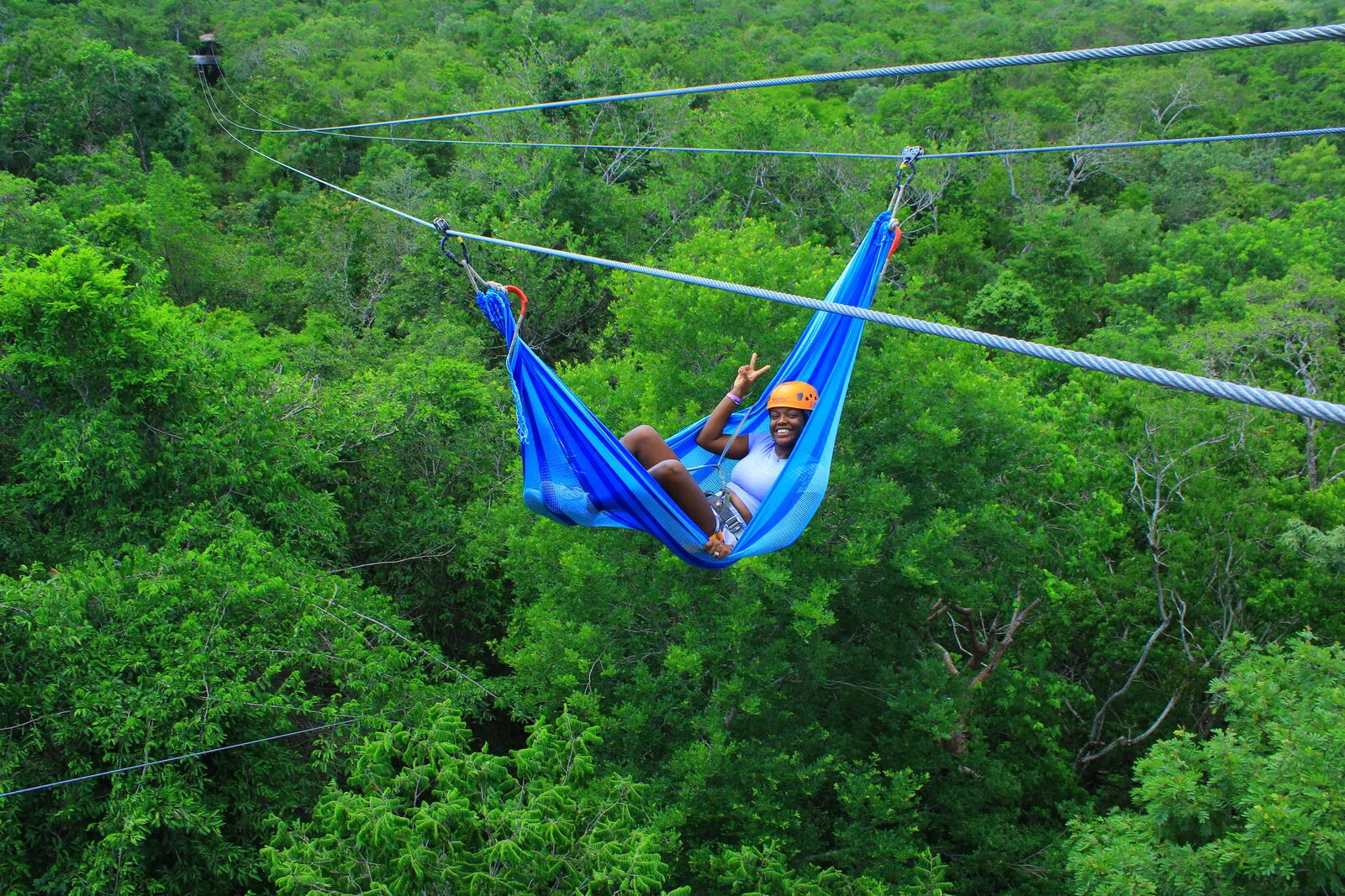 Foto original: mujer saludando desde una hamaca azul sobre la selva, en una toma cerrada sin cielo